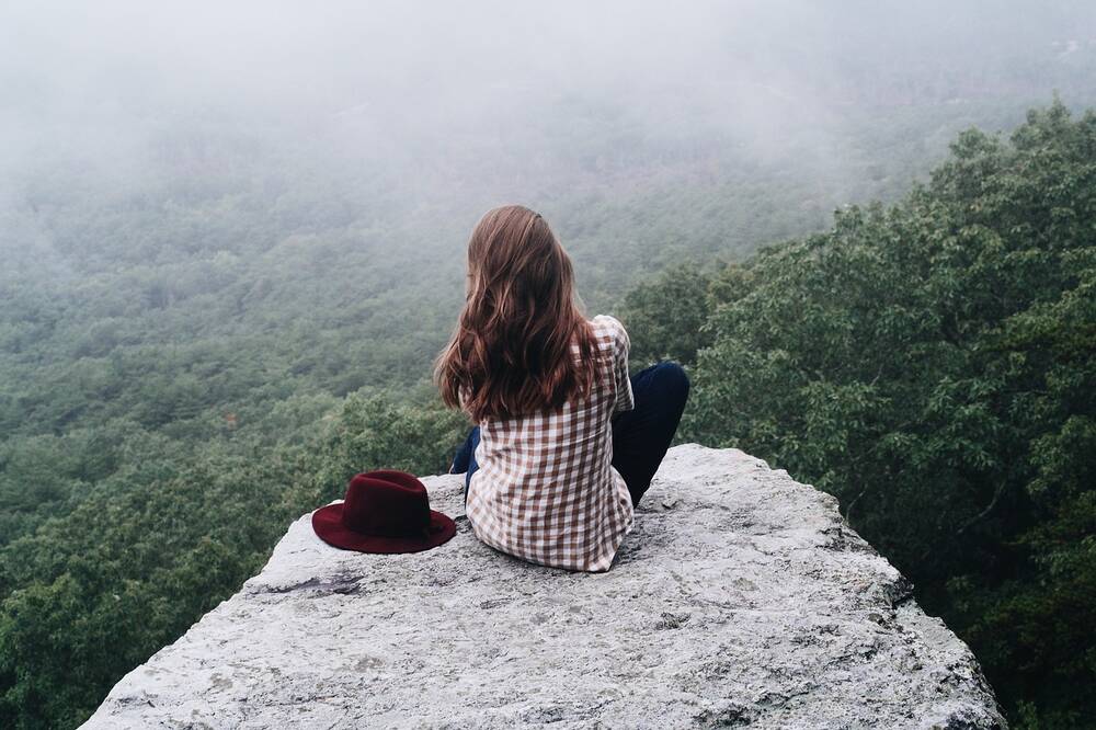 A woman sat on a rock looking down on treetops