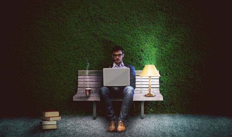 A man working on his laptop in front of a hedge