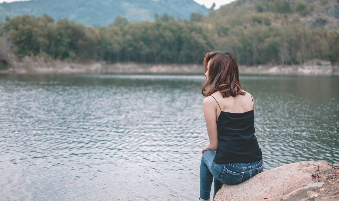 A sad woman sat looking at a lake and trees